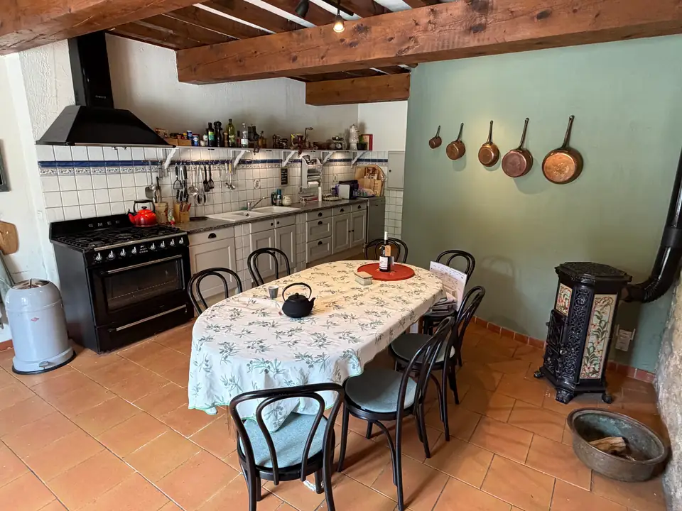 The kitchen: copper pans on the green wall, a black range, blue and white tiles and an oval table.