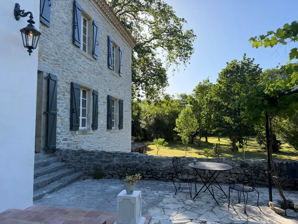 A round iron table on the terrace, with the lawn and old trees beyond the parapet.