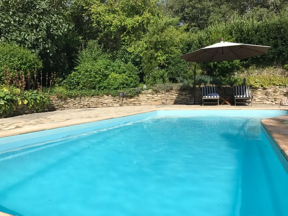 The pool, with a parasol against a stone wall on the far side.
