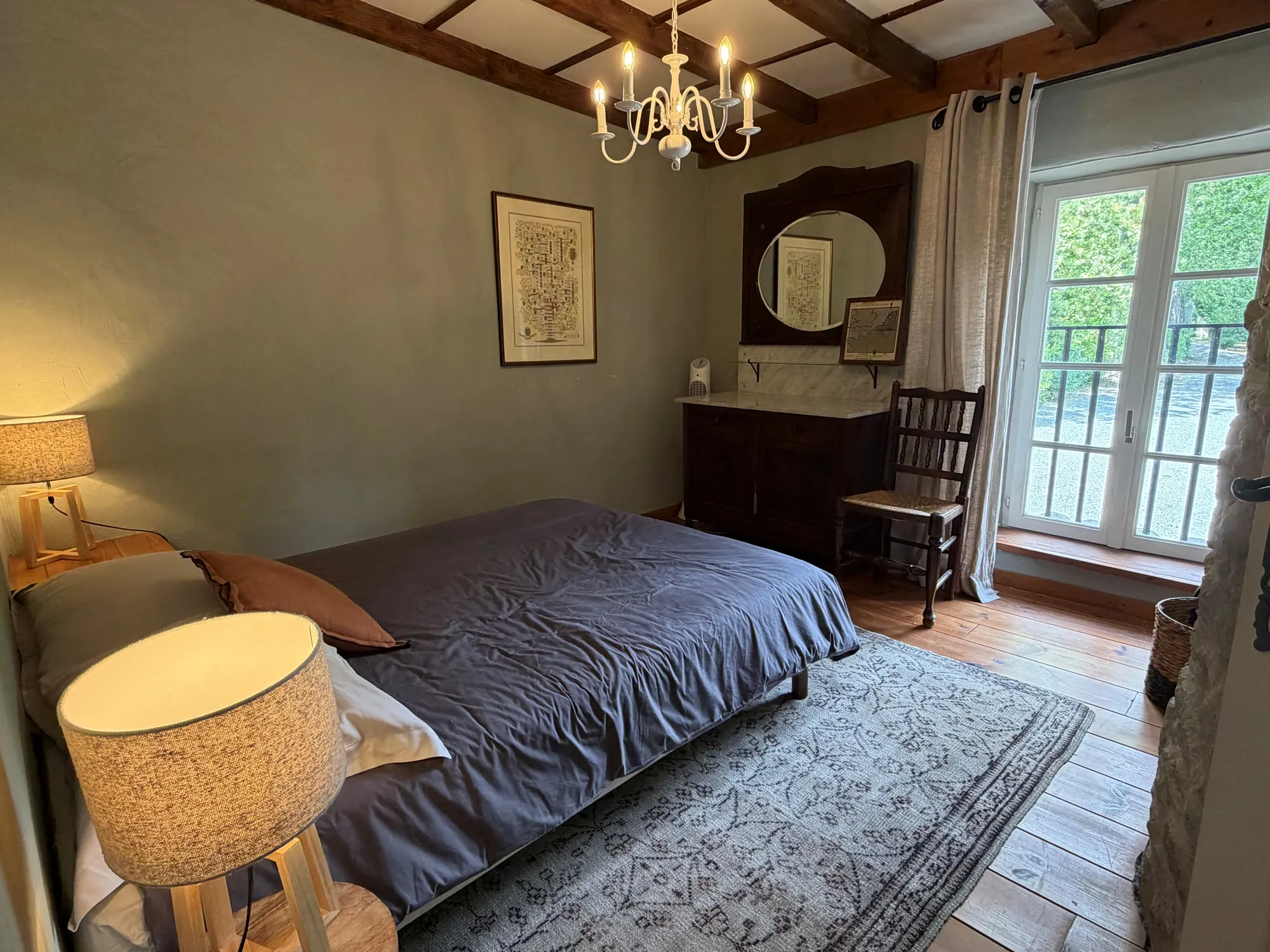Een slaapkamer met een grijs bed, balken en een kroonluchter.