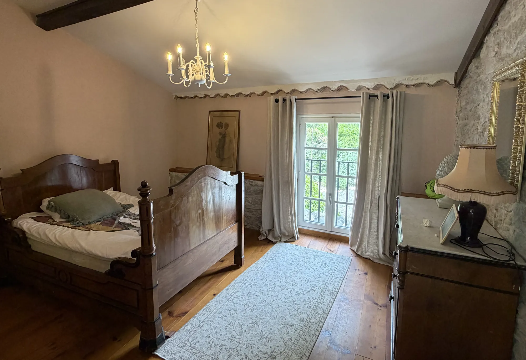 Een slaapkamer met een donker houten bed onder een kroonluchter, met deuren naar buiten.