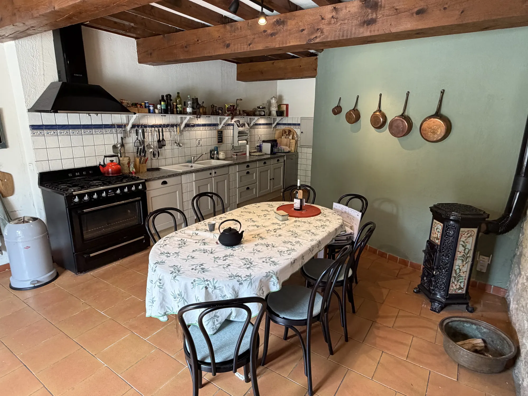 De keuken met fornuis, koperen pannen aan de wand en een tafel op de plavuizen.