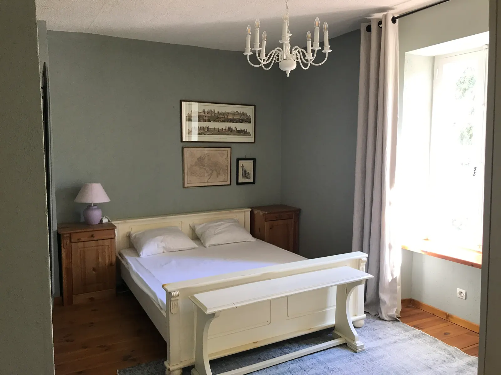 Een slaapkamer met een wit bed tegen groengrijze wanden.
