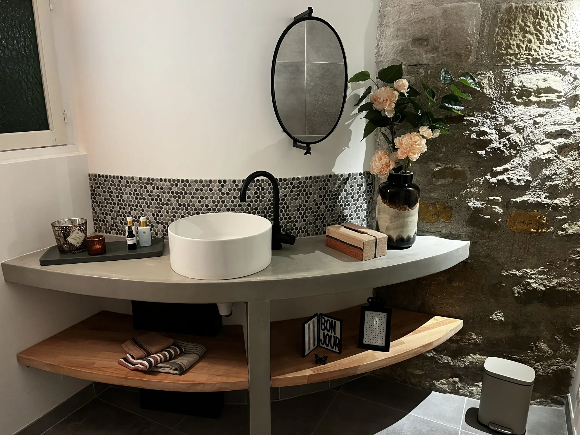 Het toilet: een ronde fontein op een houten plank tegen natuursteen.