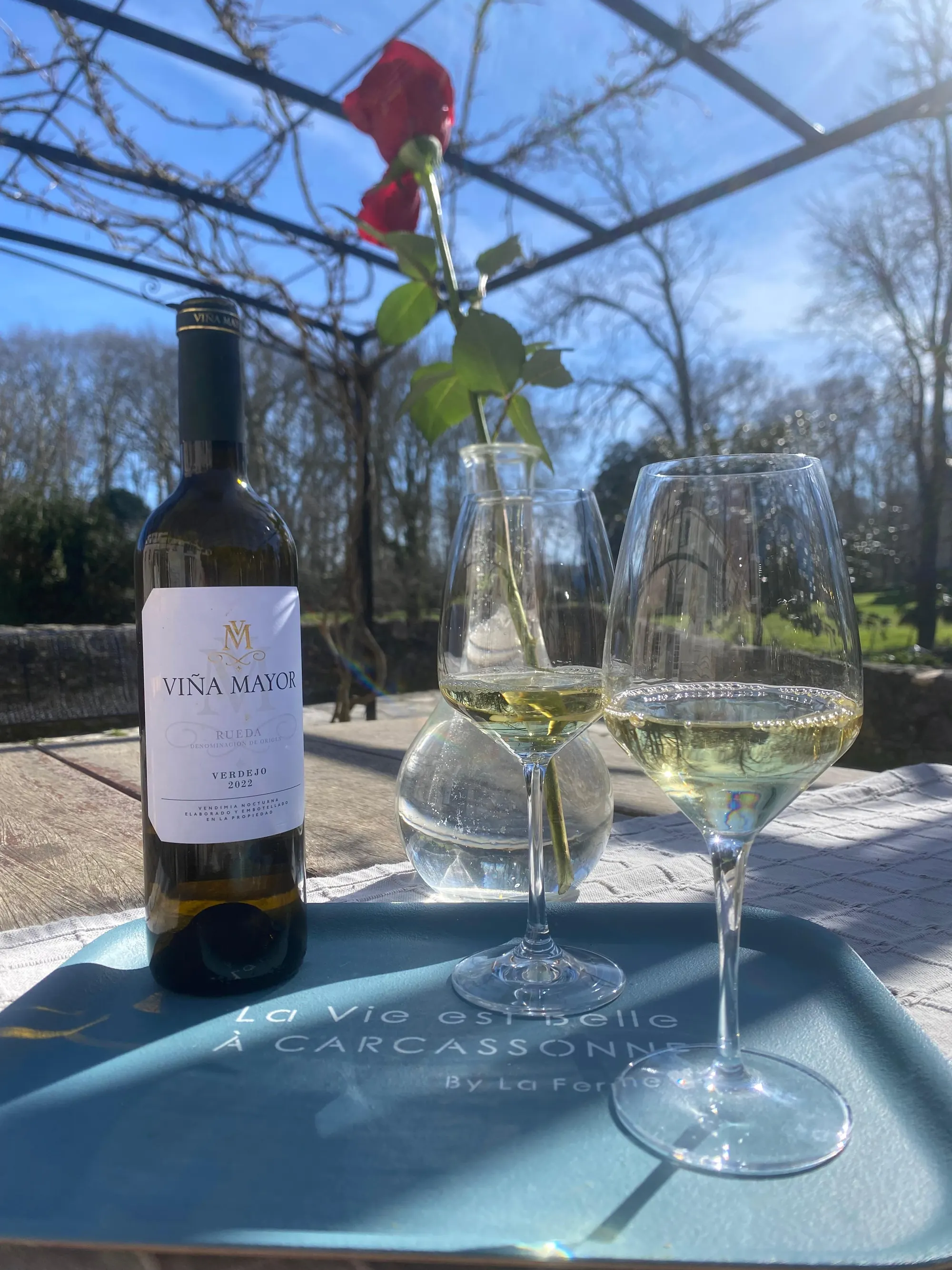 Een fles en twee glazen op een tafel onder de pergola.